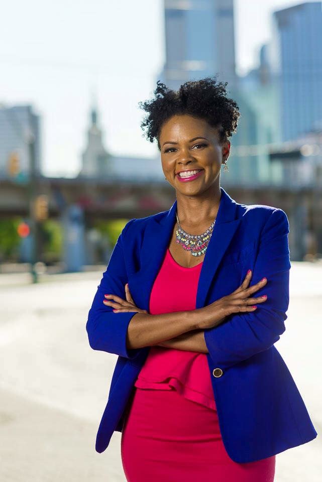 Black woman with curly natural with blue jacket and pink dress. 