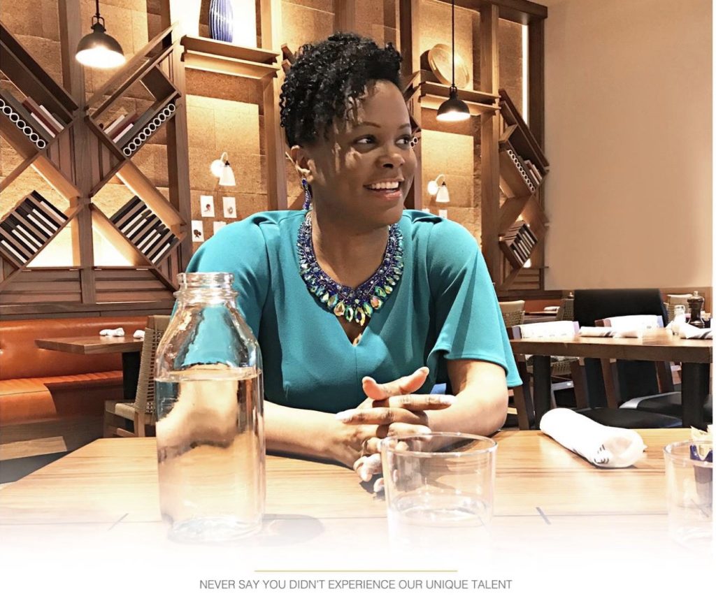 NSYDE Out Photo Black Woman with curly hair sitting at brown table with hands on the table. 