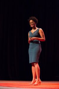 Alicia M Morgan on TEDx Plano stage with black background and green dress. The carpet is red.