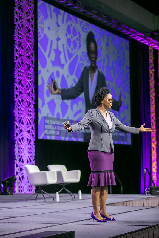 Alicia Morgan on stage during Society of Women Engineers WE23 conference. Alicia is wearing purple and gray SWE colors. Stage is also purple and gray.